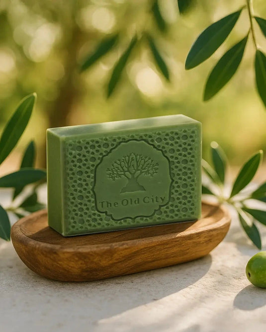 Green bar of soap on a wooden stand with olive leaves and olives on a natural background